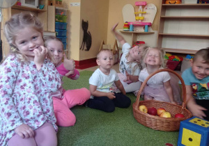 Dzieci siedzą na dywanie z koszem jabłek