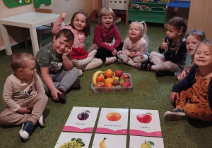 Dzieci na dywanie oglądaja ilustracje owoców.