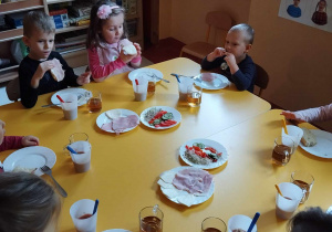 Dzieci siedzą przy stoliku i przygotowuja zdrowe kanapki.