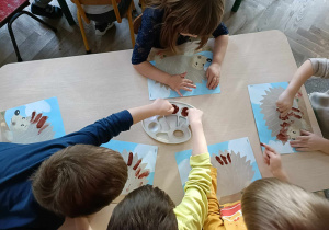 Dzieci przy stoliku malują jeże farbami.