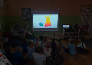 Dzieci siedzą na podłodze i oglądają animację dotycząca praw dziecka