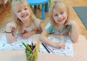 Dziewczynki siedzą przy stoliku i kolorują.