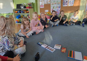 Dzieci siedzą na dywanie i wypowiadają się na temat Dnia Kredki