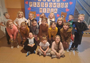 Grupa dzieci pozuje do zdjęcia na tle napisu Dzień Pluszowego Misia
