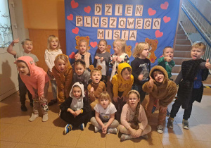 Grupa dzieci pozuje do zdjęcia na tle napisu Dzień Pluszowego Misia