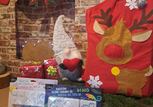 Zdjęcie upominków ufundowanych przez firmę KIDEA na tle kominka ze świątecznymi ozdobami, sanek i worka prezntów