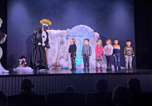 Dzieci stoją na scenie i rozmawiają z aktorem w kostiumie teatralnym