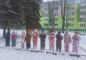 Grupa dzieci w kombinezonach zimowych pozuje do zdjecia. W rękach trzymają butelki z kolorową farbą