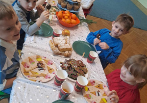 Dzieci siedzą przy stole i jedzą przekąski przygotowane przez rodziców