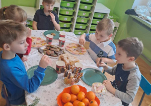 Dzieci siedzą przy stole i jedzą przekąski przygotowane przez rodziców