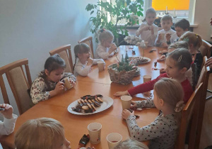 Dzieci siedzą przy stole i jedzą ciasteczka