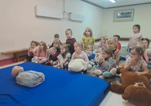 Dzieci siedzą na dywanie przed nimi na materacu leży fantom