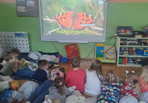 Dzieci leża na dywanie i oglądają na tablicy film edukacyjny o motylach