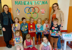 Grupa dzieci z Paniami Dyrektor pozuje do zdjęcia na tle napisu Olimpiada Matematyczna