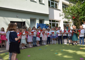 Dzieci z grupy 3 śpiewają piosenkę dla rodziców w rękach trzymają papierowe serca