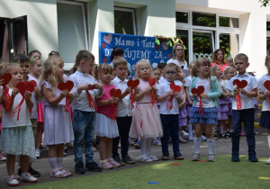 Dzieci z grupy 3 śpiewają piosenkę dla rodziców w rękach trzymają papierowe serca