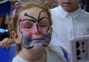 Dziewczynka z namalowanym na buzi motylem uśmiecha się do zdjęcia