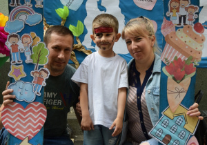 Chłopiec z rodzicami pozuje do zdjęcia w ramce z napisem Dzień Rodziny i obrazkami tematycznymi