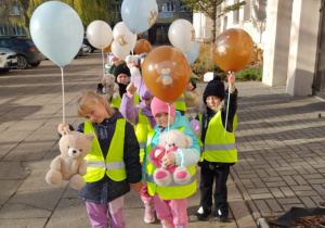 Dzieci wychodzą ze szkoły. W dłoniach trzymają misie i balony.