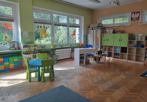 Sala przedszkolna grypy dzieci 5 letnich - stolik z krzesłami, biurko nauczyciela, szafy, dekoracje jesienne w oknach