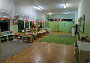 Sala przedszkolna. Po prawej stronie półki, po lewej stoliki.